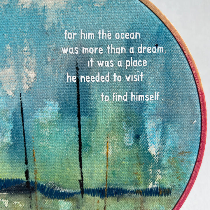 A large painted hoop art piece, with bright blues, citron green and touches of white. stitched with a deep blue shoreline and finished with the words, for him, the ocean was more than a dream. it was a place he needed to visit to find himself. 