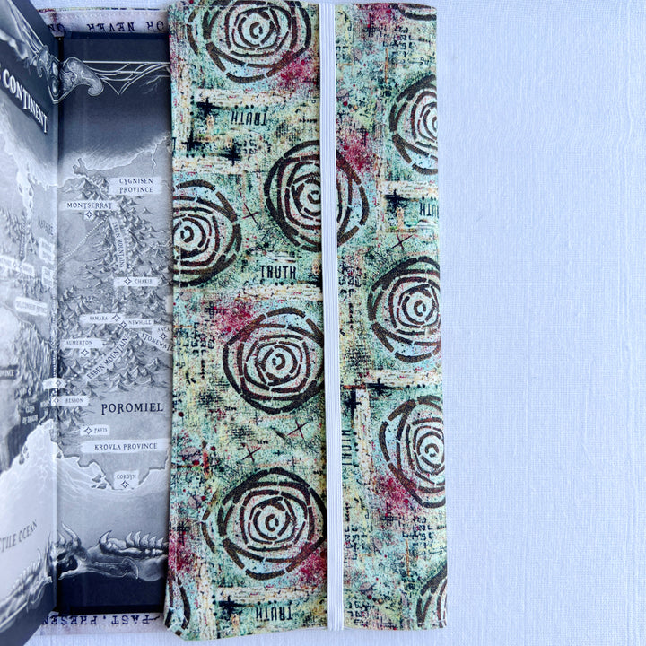 a book covered in a vibrant blue green fabric reusable  adjustable book cover.  Fabric has impressionist rose / concentric deep brown circles and the word ' TRUTH scattered on the pattern.