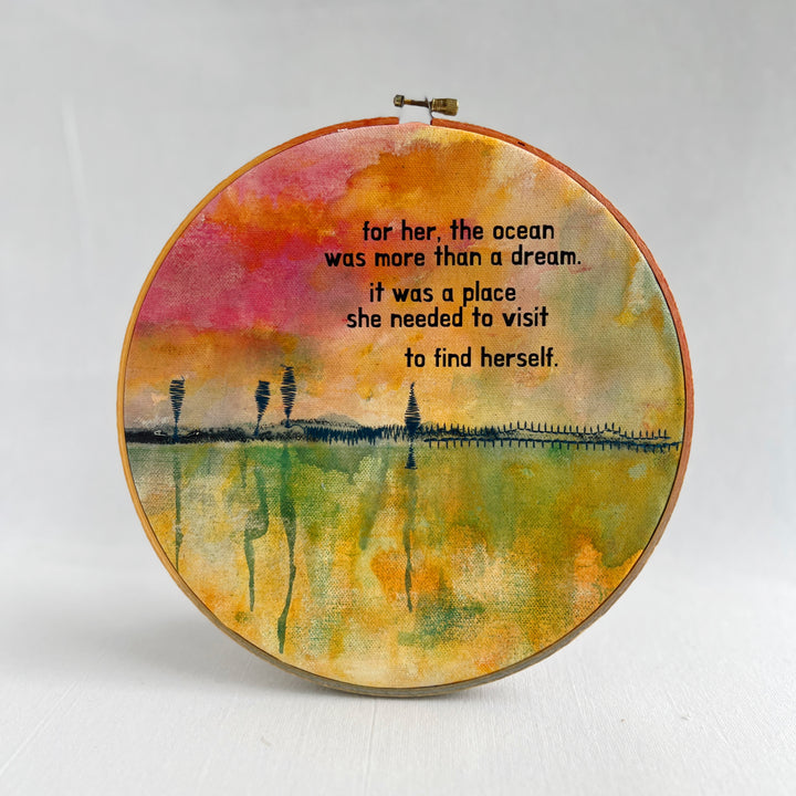 A large painted hoop art piece, with rose pinks, fresh greens and vibrant yellows, stitched with a rickety pier and finished with the words, for here, the ocean was more than a dream. it was a place she needed to visit to find herself.