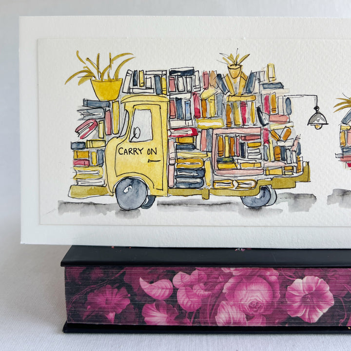 A rectangular watercolor painting of two yellow book trucks stacked and overloaded with books and potted plants, plus a wonky book light, all displayed on top of a decorative pink floral book  against a white background.