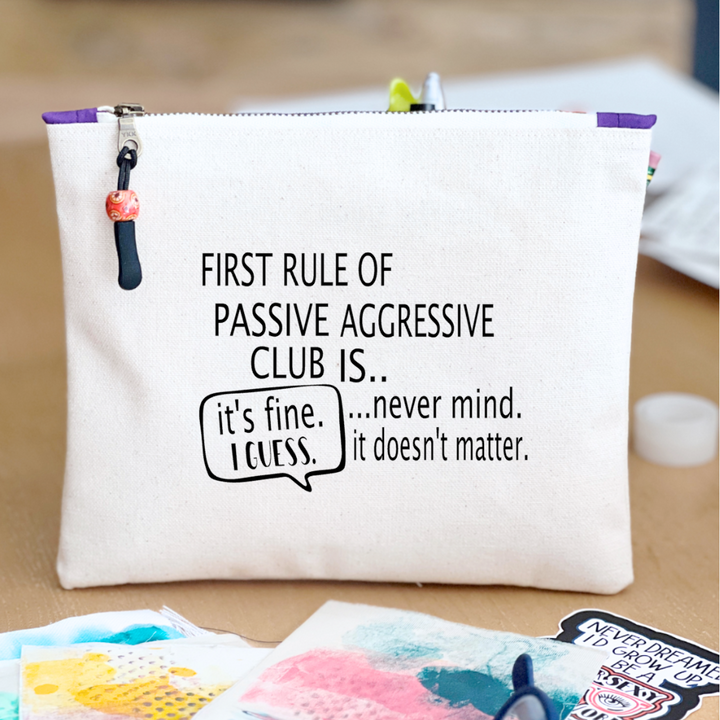 a canvas zip bag with blue watercolor painting and the words, "First rule of passive aggressive club is..never mind. it doesn't matter. it's fine. I guess."