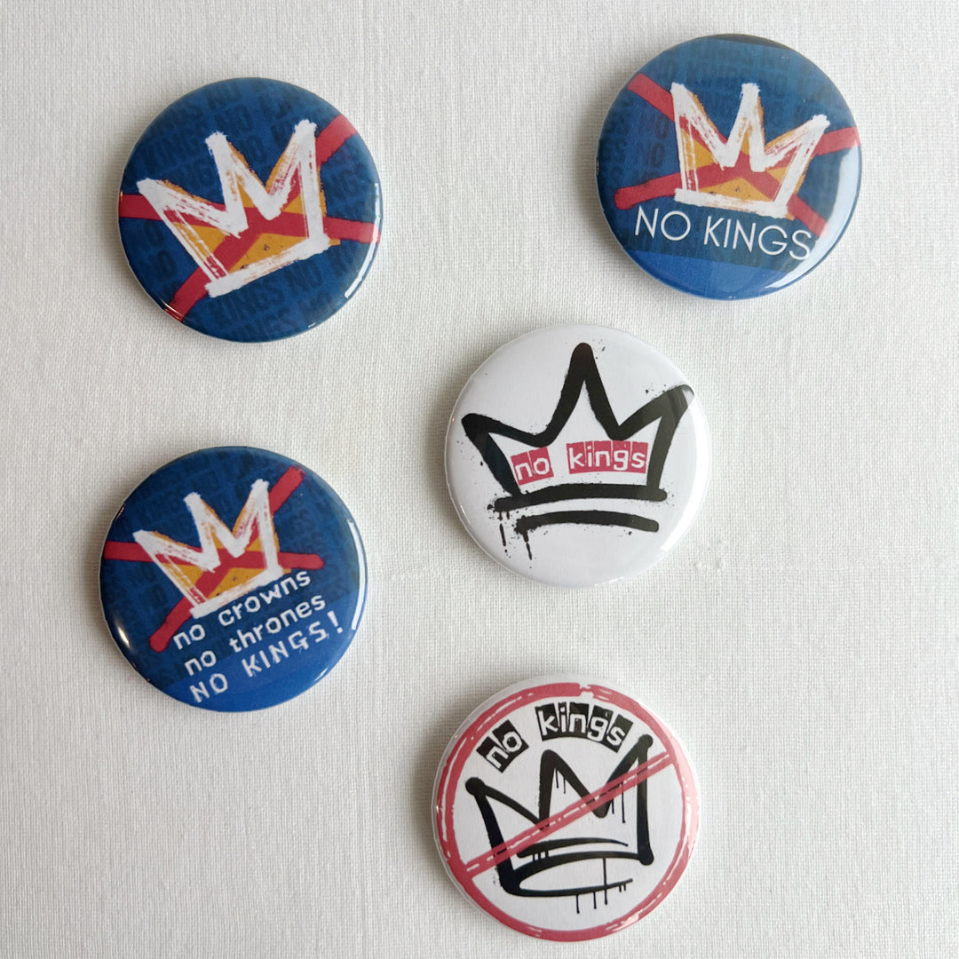 five pinback buttons in shades of blue, red and black, all signifying a 'no kings' message.