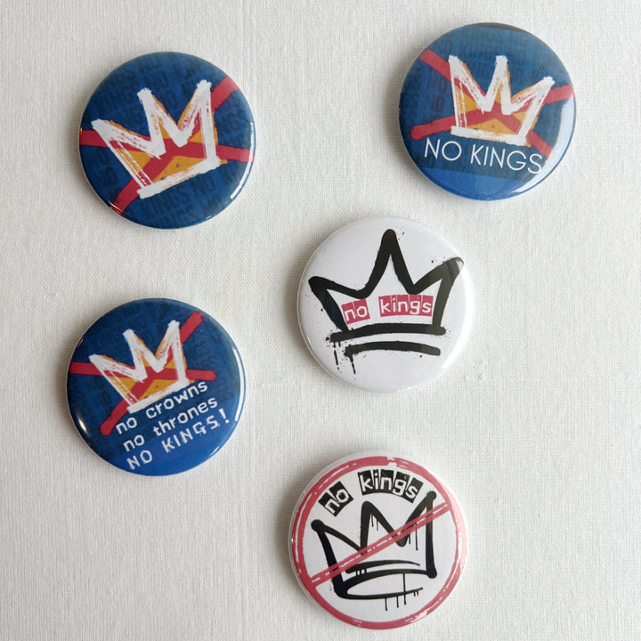 five pinback buttons in shades of blue, red and black, all signifying a 'no kings' message.