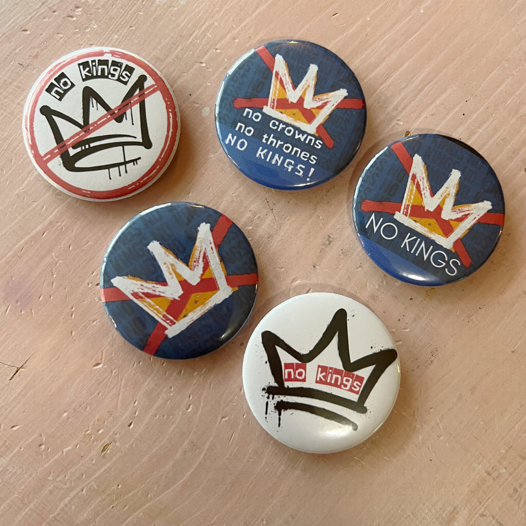 five pinback buttons on a pink background in shades of blue, red and black, all signifying a 'no kings' message.