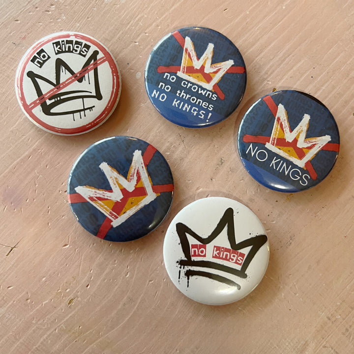 five pinback buttons on a pink background in shades of blue, red and black, all signifying a 'no kings' message.