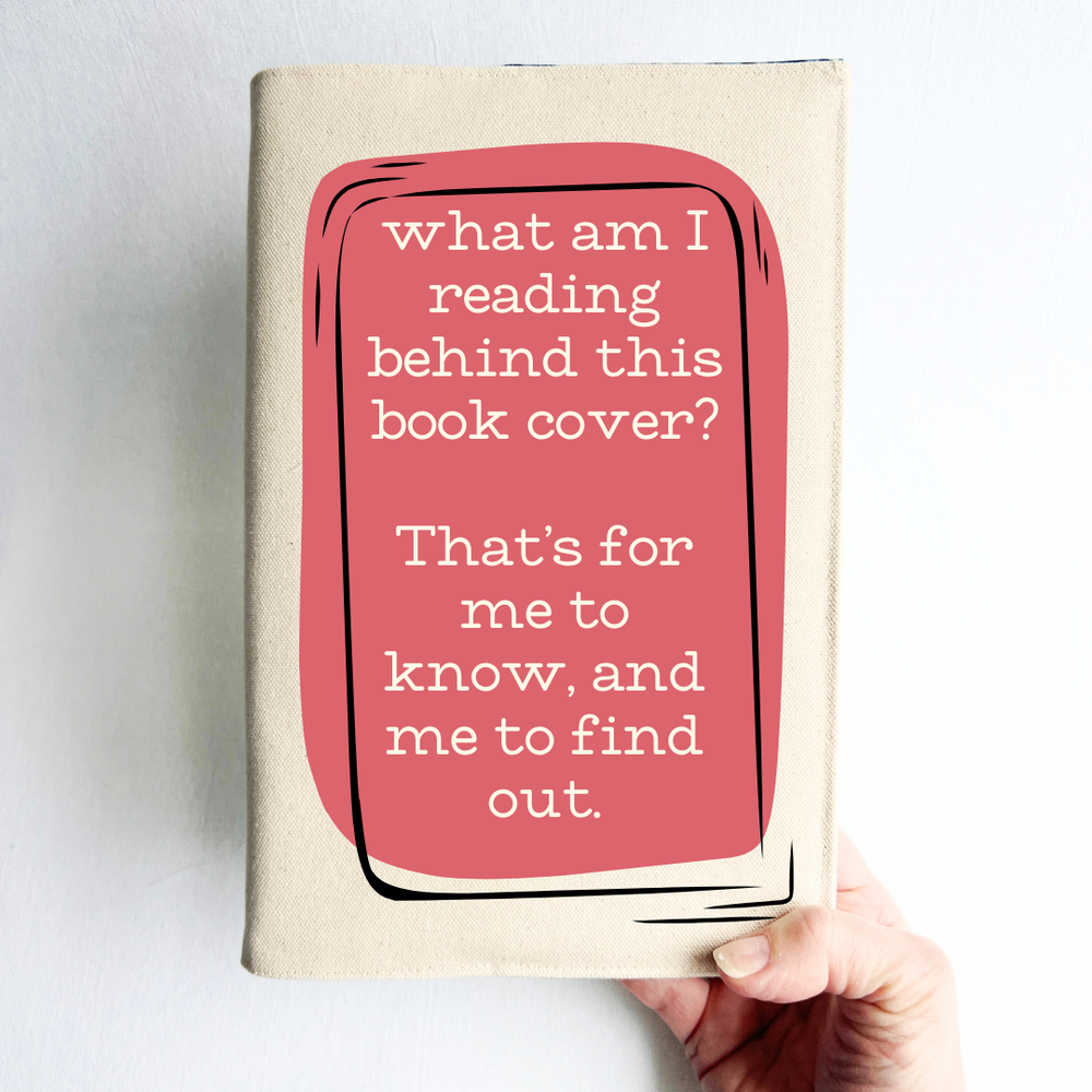 A hand holding a book covered with a reusable canvas book cover in linen, with the words, 'what am I reading behind this book cover?  That's for me to know, and me to find out' in cream lettering, placed on a rectangular coral box design.