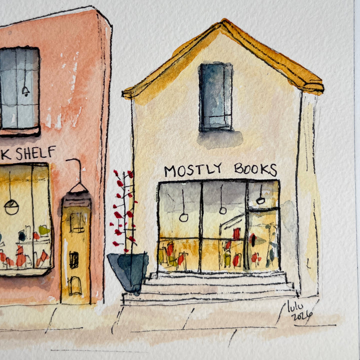 A watercolor art print depicting four stone bookstore buildings, presented with a wide white mat board against a neutral gray background.