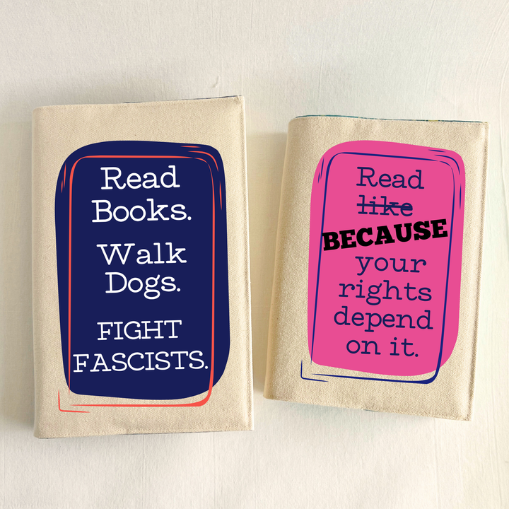 Canvas, reusable book covers in linen, with the words, 'Read Books. Walk Dogs. FIGHT FASCISTS.'  in white lettering placed on a rectangular navy box design on one cover, and 'Read like (because) your rights depend on it' in navy lettering on a pink box design.