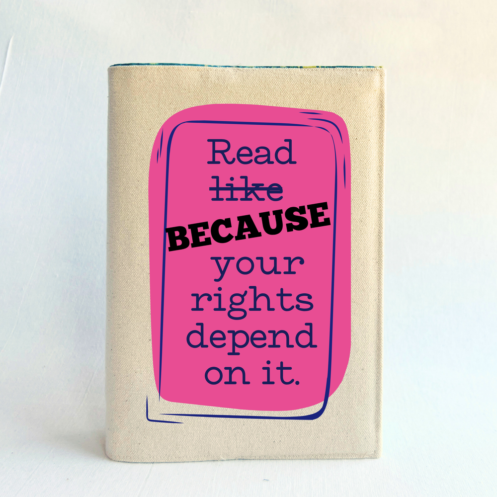 Canvas, reusable book cover in linen, with the words,  'Read like (because) your rights depend on it' in navy lettering on a pink box design.