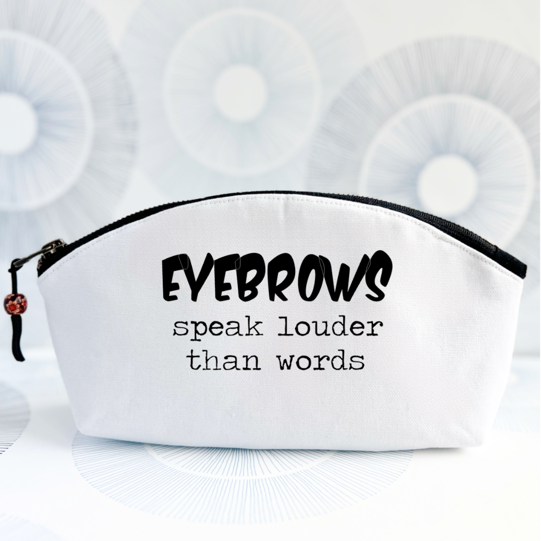 white canvas cosmetic bag with a curvy top, black zipper and the words, eyebrows speak louder than words.