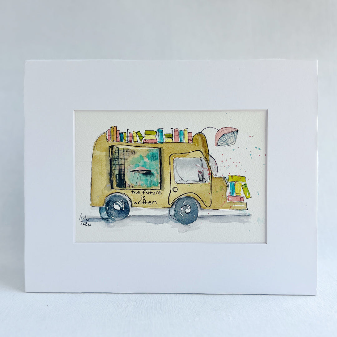 A matted watercolor painting of a mustard-yellow sci-fi book truck carrying colorful books, with the text 'the future is written' on the side, shown against a white mat and light wall background.