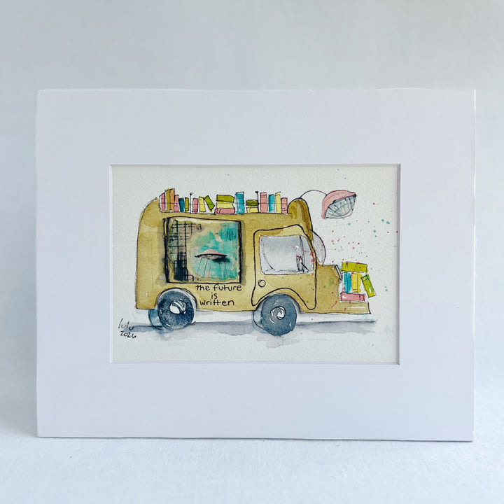 A matted watercolor painting of a mustard-yellow sci-fi book truck carrying colorful books, with the text 'the future is written' on the side, shown against a white mat and light wall background.