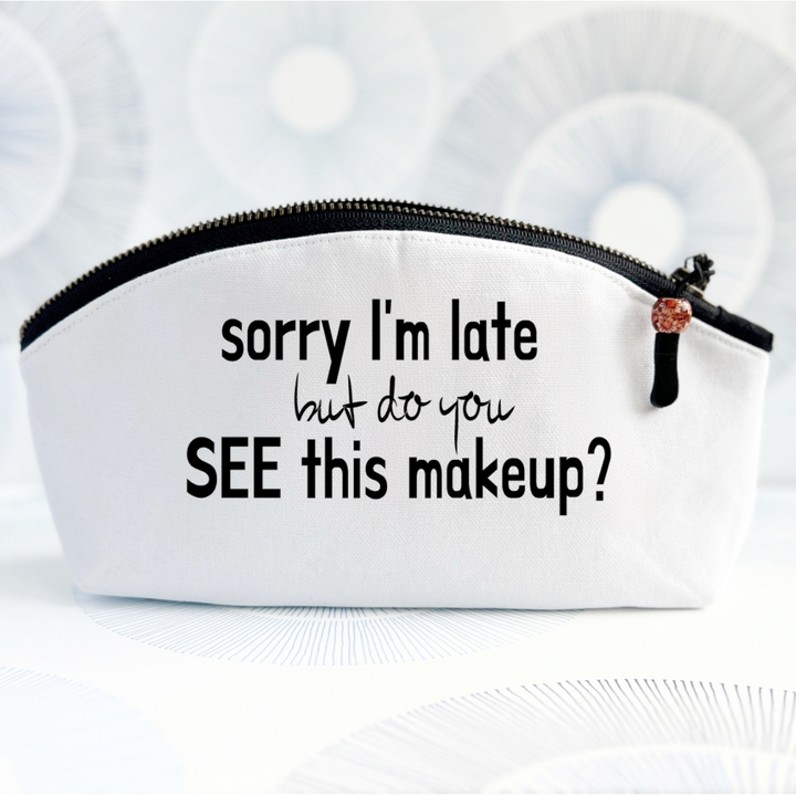 white canvas zip bag with black zipper, curved top and the words, sorry I'm late but do you see this makeup?