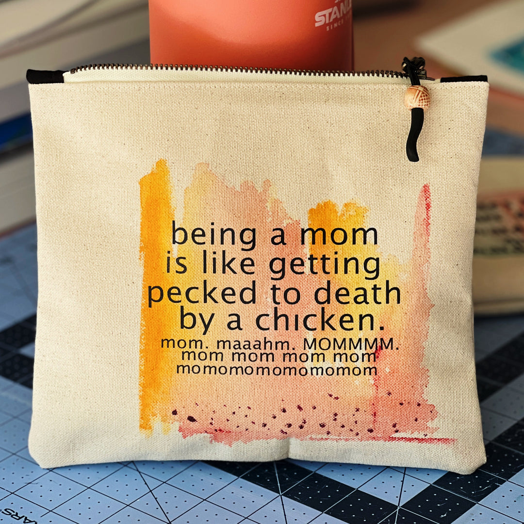 canvas zip bag measuring 9x7 inches, with orange yellow and rose watercolor paints and the words, "being a mom is like getting pecked to death by a chicken. mom. maahm. MOMMMMM!" in black lettering.