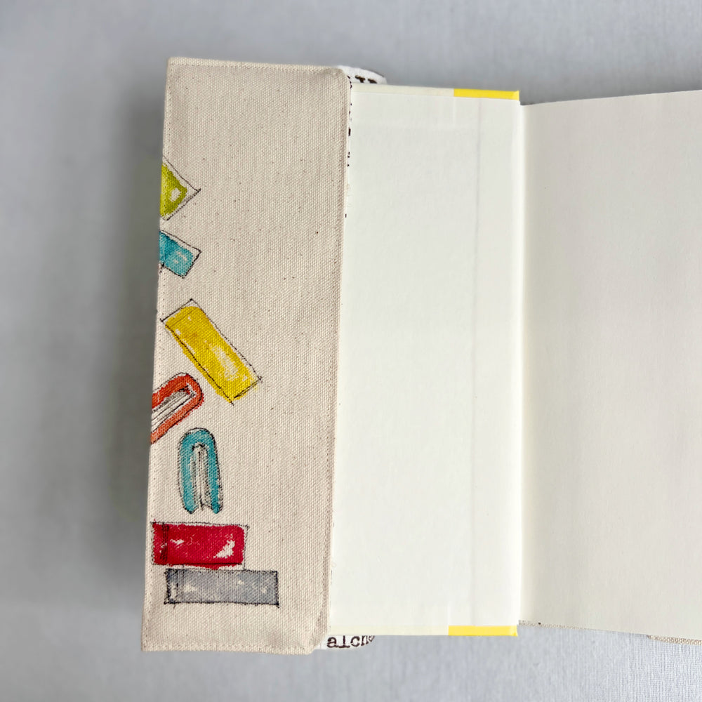 An open canvas book cover featuring colorful watercolor books illustrated on the left side, photographed against a neutral gray background.