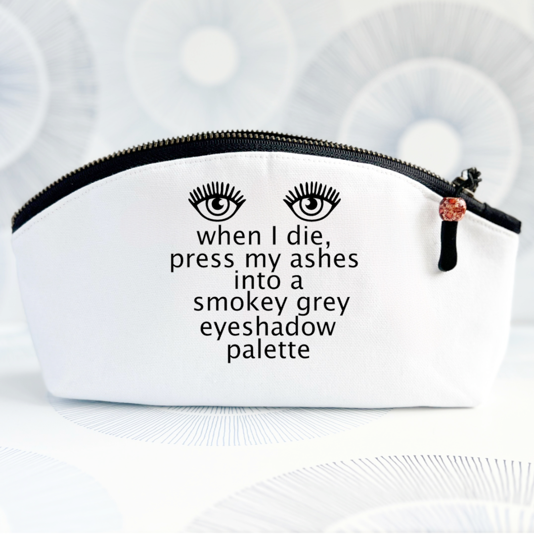 white canvas bag with curved top and black zipper, with the words, when I die, press my ashes into a smokey grey eyeshadow palette