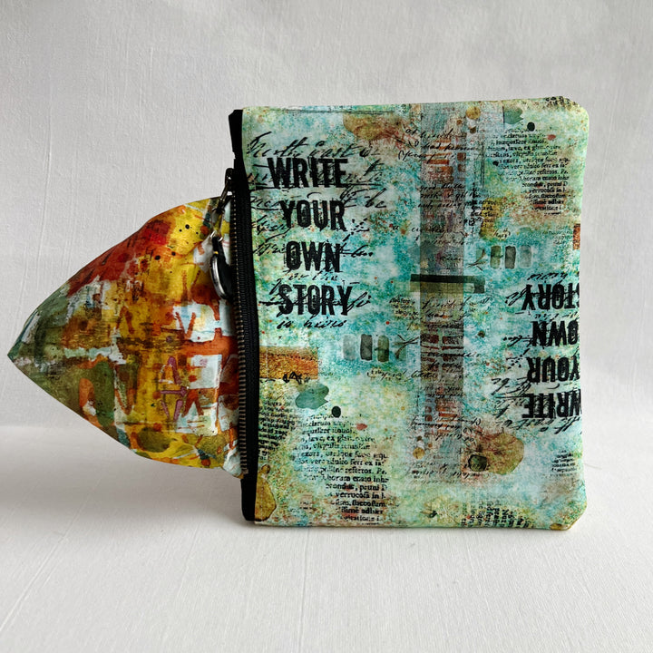 padded canvas zip bag with a mix of green and blue fabric and the words, Write Your Own Story, plus a colorful zipper pull and lining