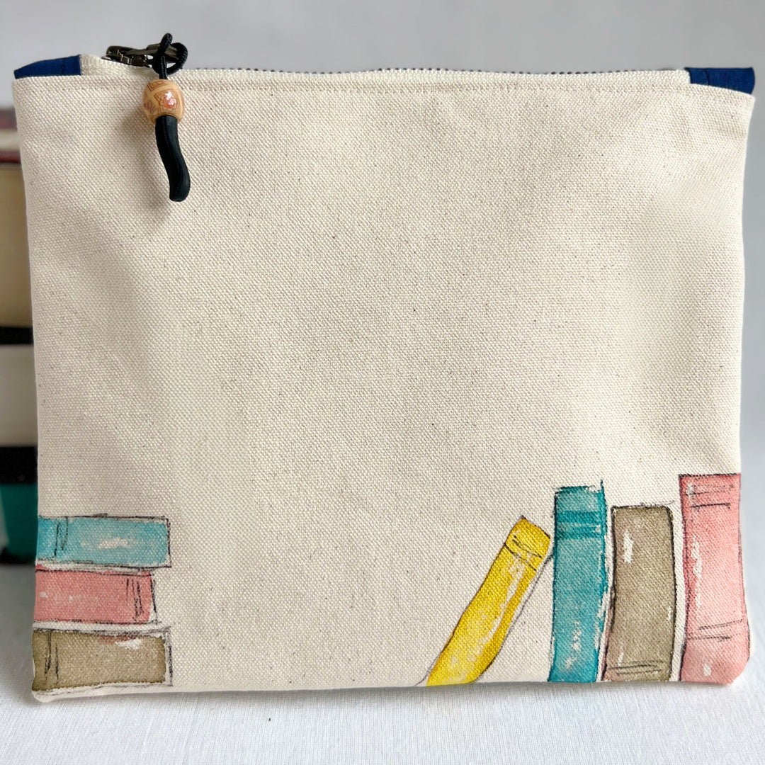 An off-white canvas zippered pouch with original watercolor painted colorful books along the bottom edge.