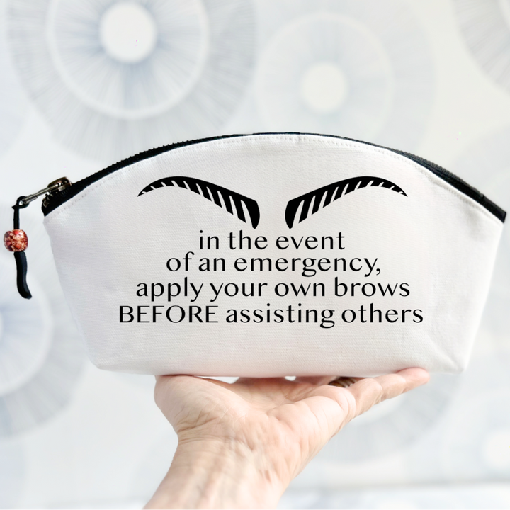 white canvas bag with black zipper, strong eyebrows and the words, in the event of an emergency, apply your own brows BEFORE assisting others