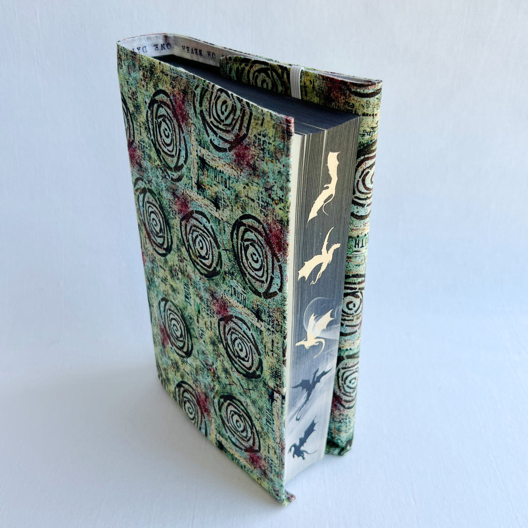 a book covered in a vibrant blue green fabric reusable  adjustable book cover.  Fabric has impressionist rose / concentric deep brown circles and the word ' TRUTH scattered on the pattern.