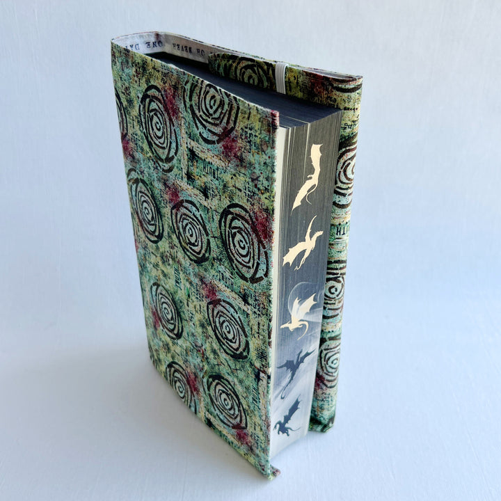 a book covered in a vibrant blue green fabric reusable  adjustable book cover.  Fabric has impressionist rose / concentric deep brown circles and the word ' TRUTH scattered on the pattern.