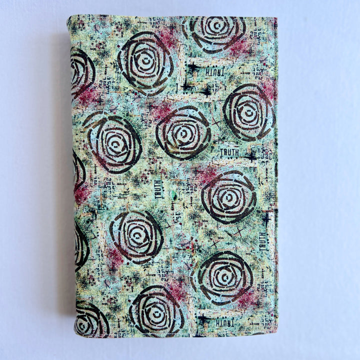 a book covered in a vibrant blue green fabric reusable  adjustable book cover.  Fabric has impressionist rose / concentric deep brown circles and the word ' TRUTH scattered on the pattern.