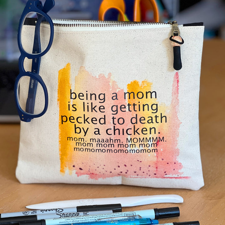 canvas zip bag measuring 9x7 inches, with orange yellow and rose watercolor paints and the words, "being a mom is like getting pecked to death by a chicken. mom. maahm. MOMMMMM!" in black lettering.