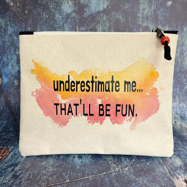 a canvas zip bag with watercolor paints and the words, "underestimate me, that'll be fun" in black lettering