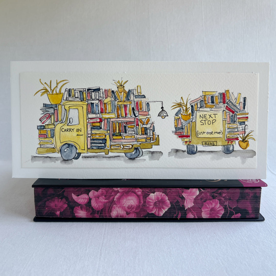 A rectangular watercolor painting of two yellow book trucks stacked and overloaded with books and potted plants, plus a wonky book light, all displayed on top of a decorative pink floral book  against a white background.