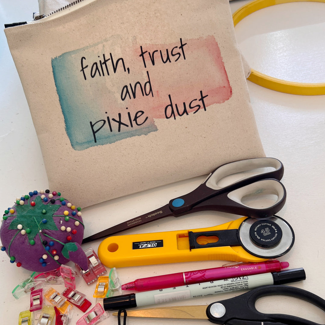 square canvas zip bag with the words faith, trust and pixie dust. office and sewing supplies to demo how much stuff will fit in the bag.