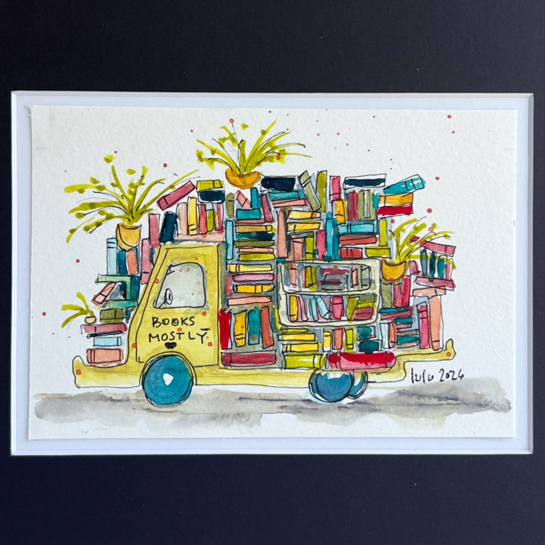 A framed watercolor illustration of a yellow book truck covered with colorful books and potted plants, with the text 'BOOKS MOSTLY' on the side, shown against a dark background.