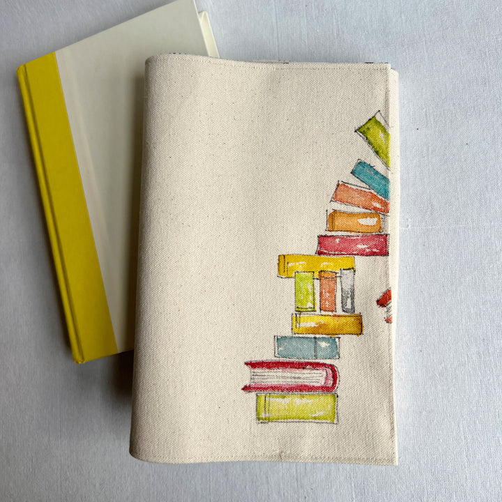 A canvas linen book cover featuring a hand-painted stack of colorful books on the right side, resting on a book