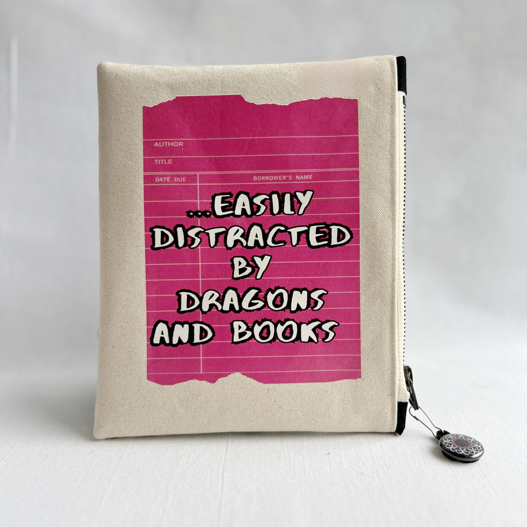 padded canvas zip bag with a coral red library card and the words, easily distracted by books and dragons, plus a colorful zipper pull and lining