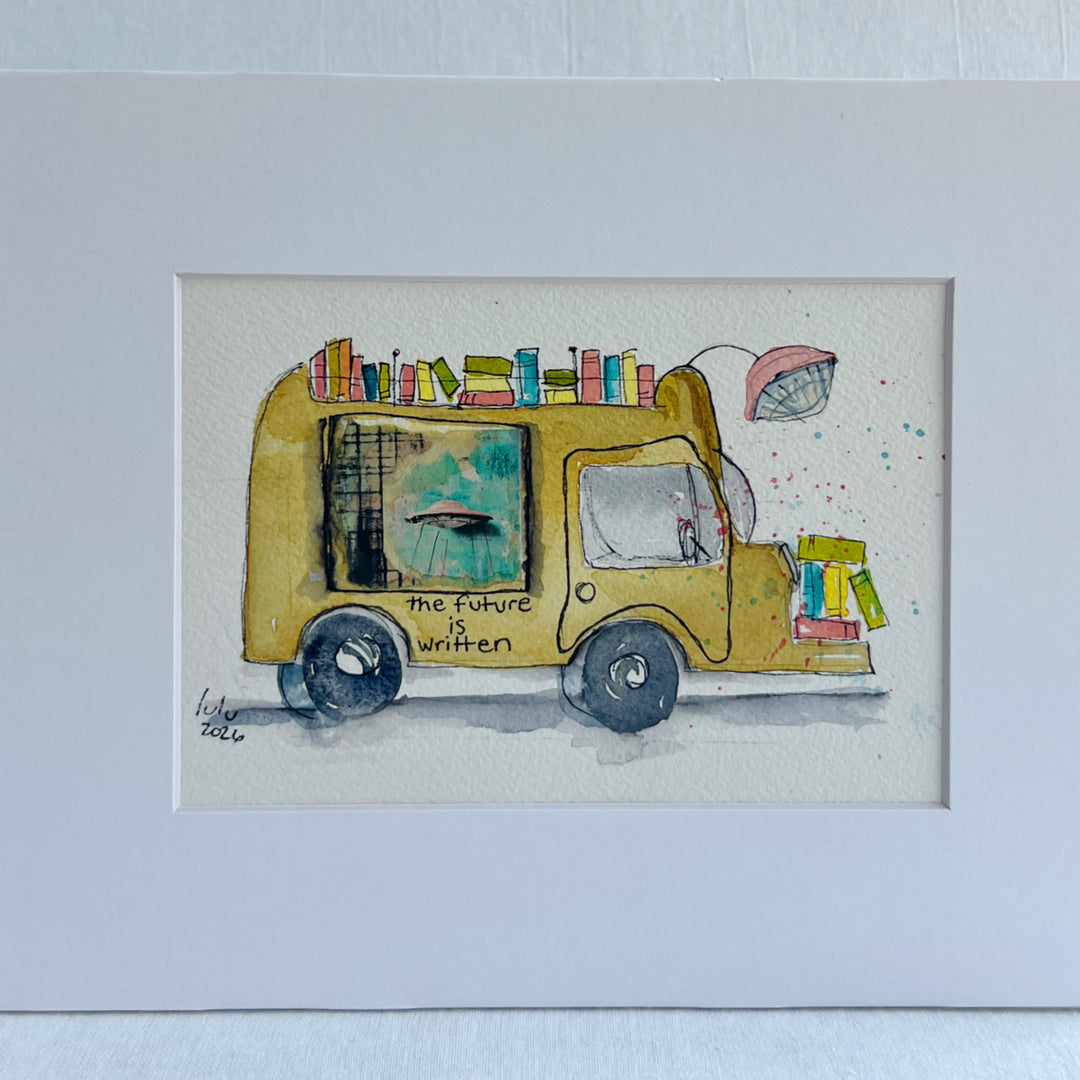 A matted watercolor painting of a mustard-yellow sci-fi book truck carrying colorful books, with the text 'the future is written' on the side, shown against a white mat and light wall background.