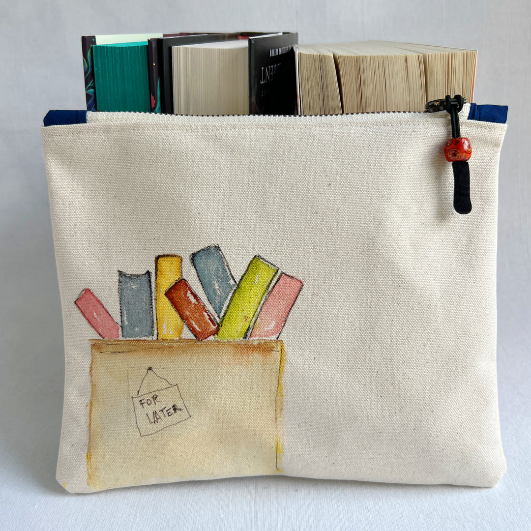 A canvas zippered pouch with a watercolor illustration of colorful books in a box labeled 'FOR LATER'. Several books are tucked inside the pouch, which is photographed against a light gray background.