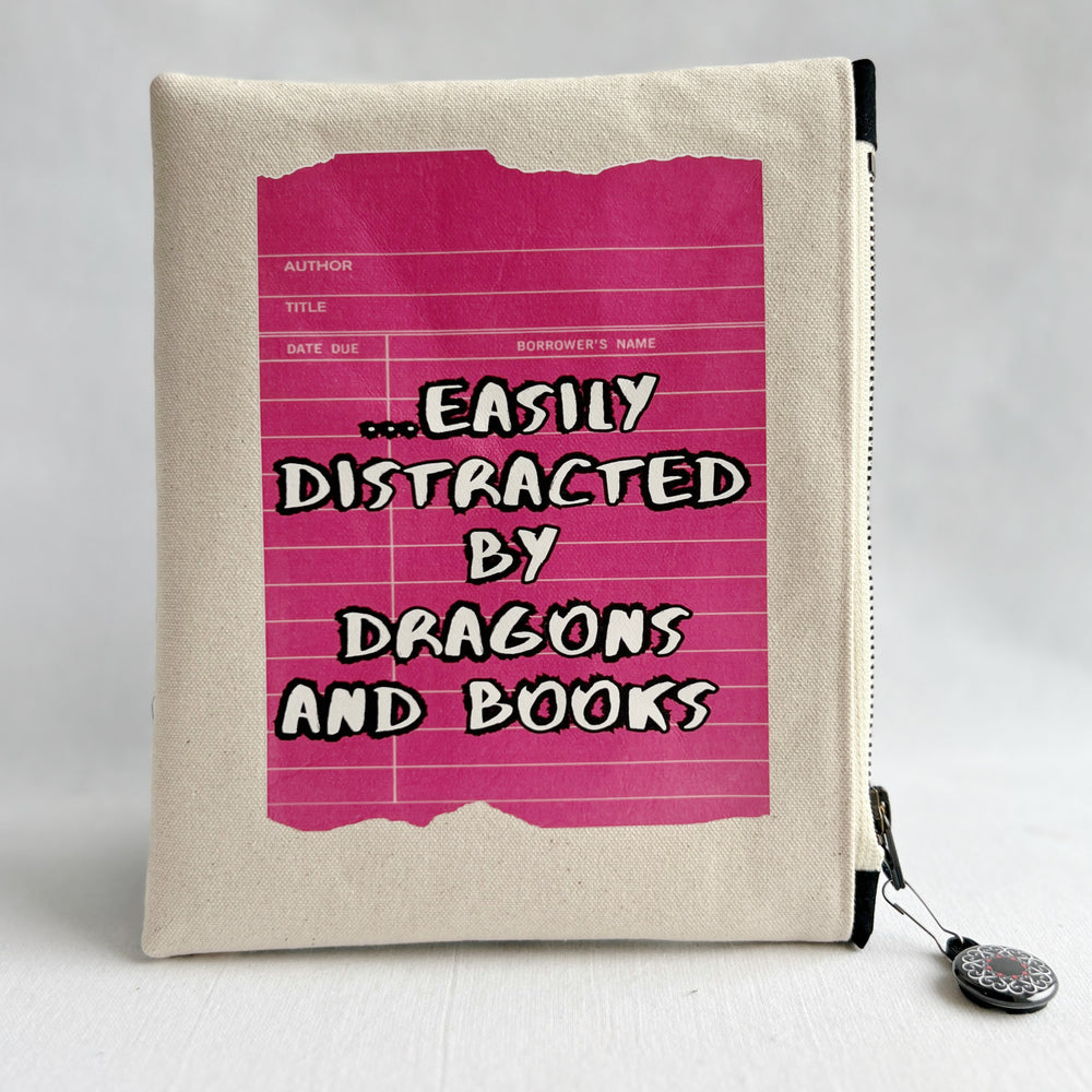 padded canvas zip bag with a coral red library card and the words, easily distracted by books and dragons, plus a colorful zipper pull and lining