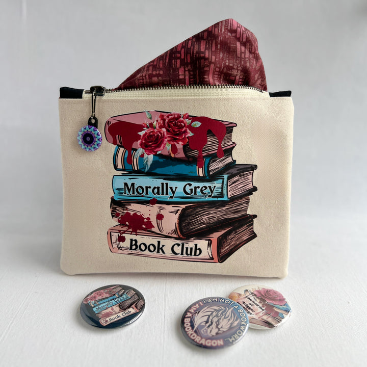 square canvas bag with colorful zipper pull, and a design on the front with a stack of books, some roses, blood spatters and drips and the words, "Morally grey book club."