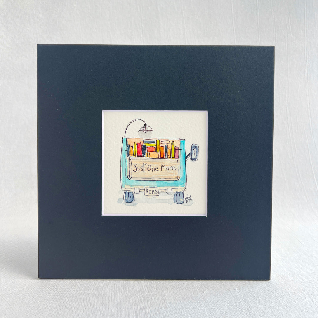 A square original watercolor art print depicting the back end of a blue pickup truck loaded with colorful books and a wonky reading light, with the words, "Just One More' and a license plate with the word 'Read'