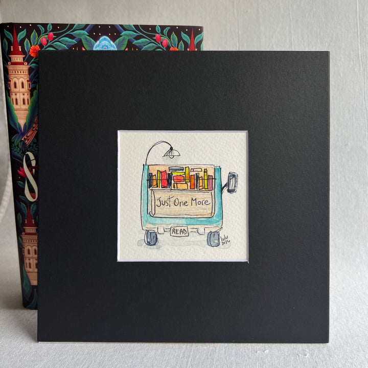 A square original watercolor art print depicting the back end of a blue pickup truck loaded with colorful books and a wonky reading light, with the words, "Just One More' and a license plate with the word 'Read'