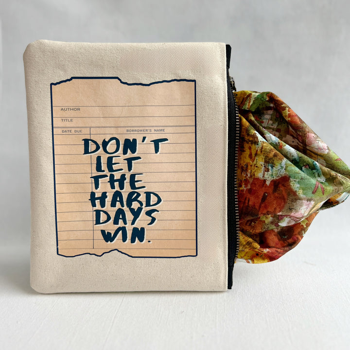 padded canvas zip bag with a green library card and the words, Don't Let the Hard Days Win, plus a colorful zipper pull and lining