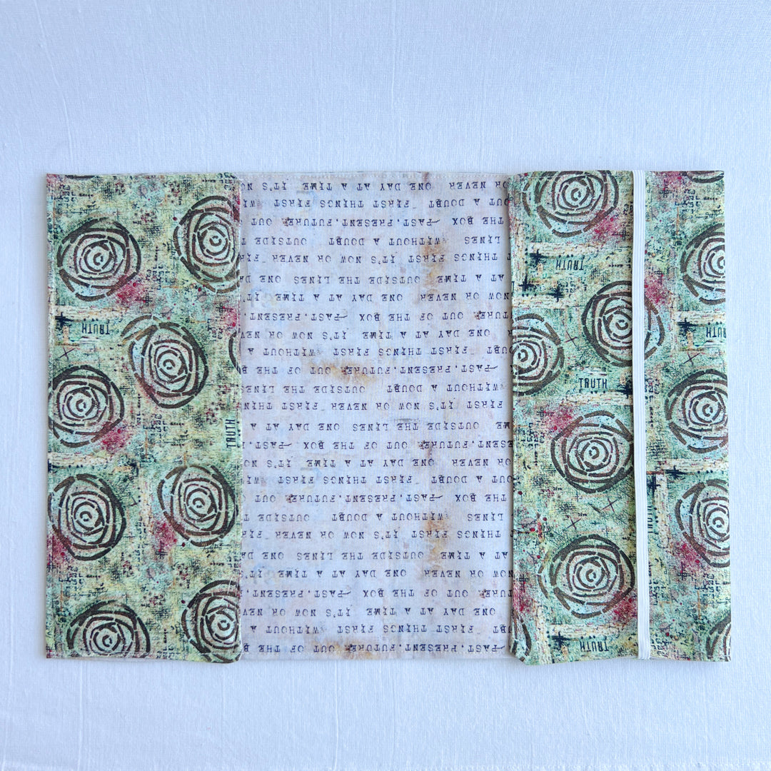 a book covered in a vibrant blue green fabric reusable  adjustable book cover.  Fabric has impressionist rose / concentric deep brown circles and the word ' TRUTH scattered on the pattern.
