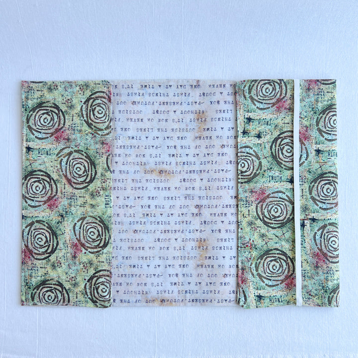 a book covered in a vibrant blue green fabric reusable  adjustable book cover.  Fabric has impressionist rose / concentric deep brown circles and the word ' TRUTH scattered on the pattern.