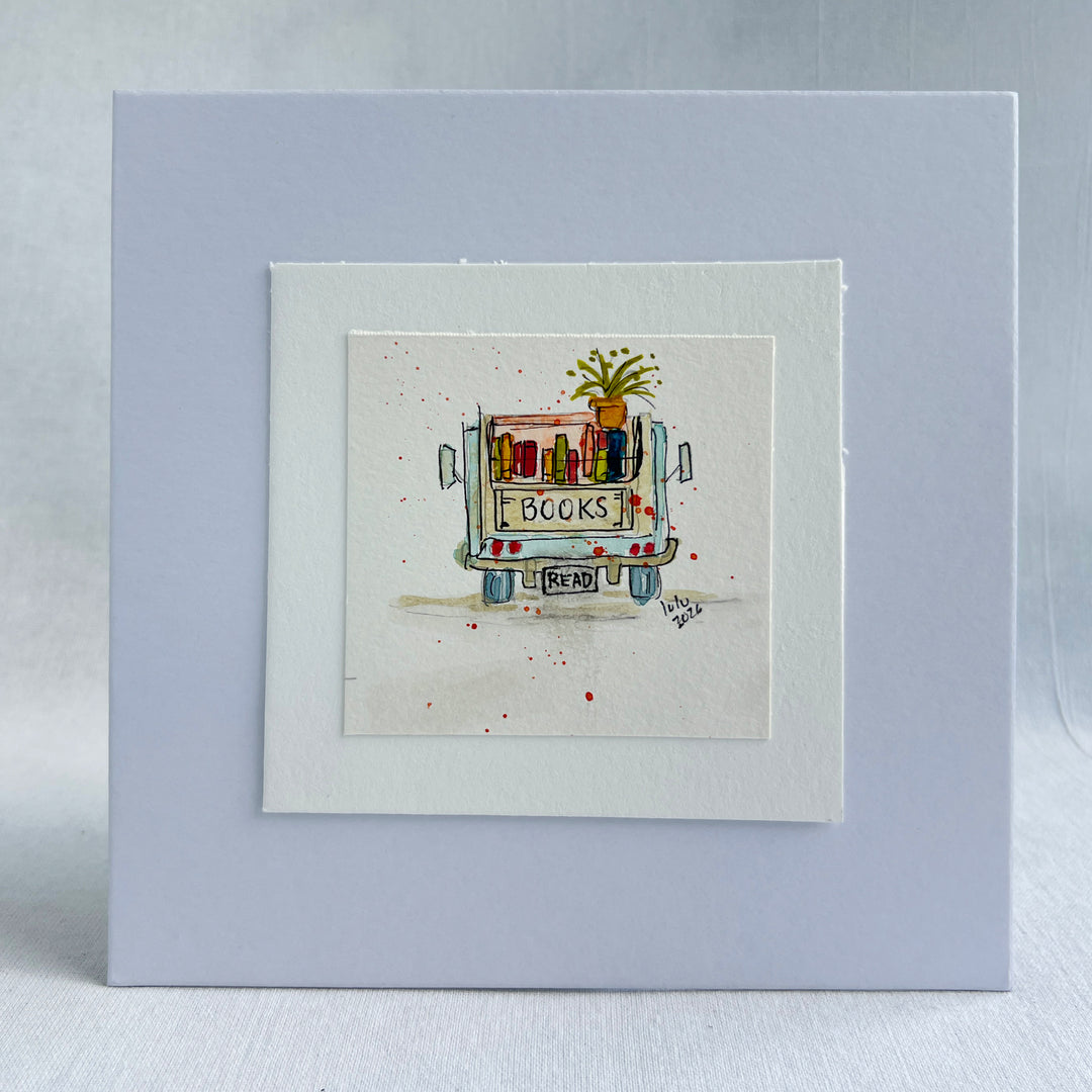 A square watercolor original art print featuring a hand-drawn and hand-painted illustration of a book cart with the word 'BOOKS' on the back and a small plant on top, displayed upright on stacked books.