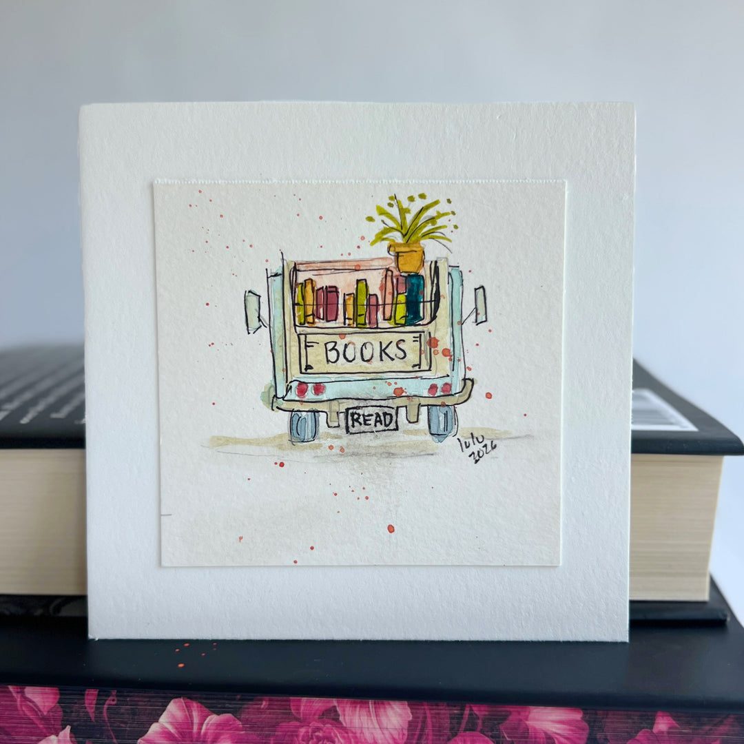 A square watercolor original art print featuring a hand-drawn and hand-painted illustration of a book cart with the word 'BOOKS' on the back and a small plant on top, displayed upright on stacked books.