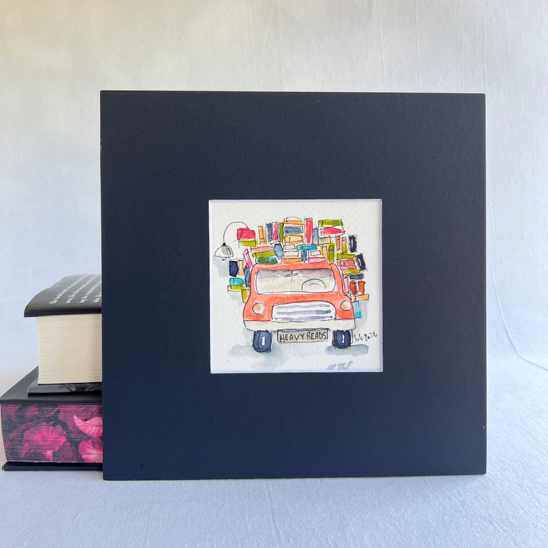 A square original watercolor art print depicting a red pickup truck loaded with colorful books and a wonky reading light, with the license plate reading 'HEAVY READS' 