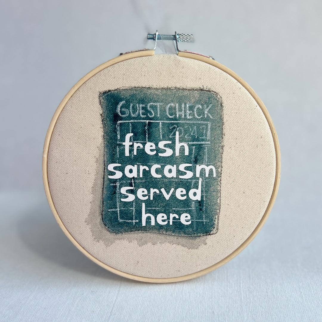 original hoop art piece with a faded guest check ticket painted in mayan blue, with the words, fresh sarcasm served here, in white vinyl lettering