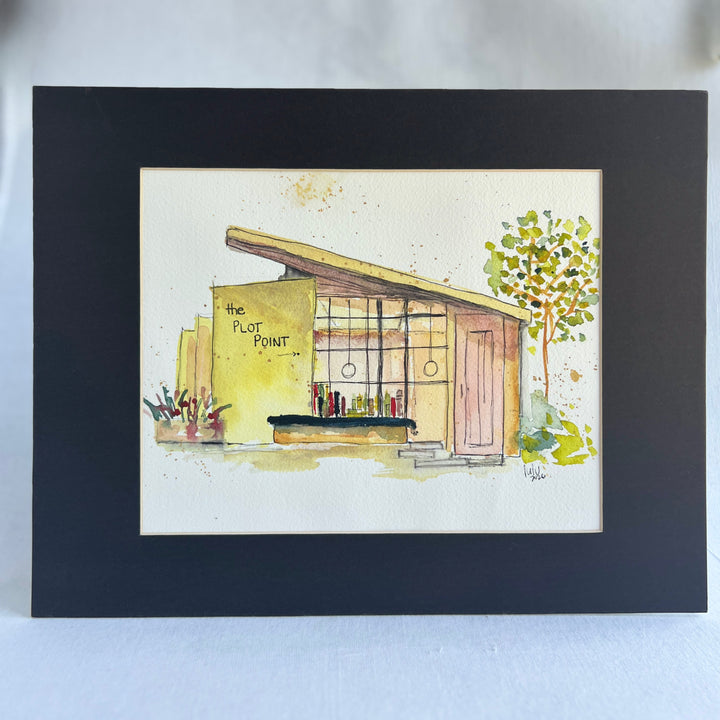 A watercolor painting of a midcentury modern bookstore with the text 'the PLOT POINT' on the yellow wall, shown on a white paper sheet against a dark navy background.