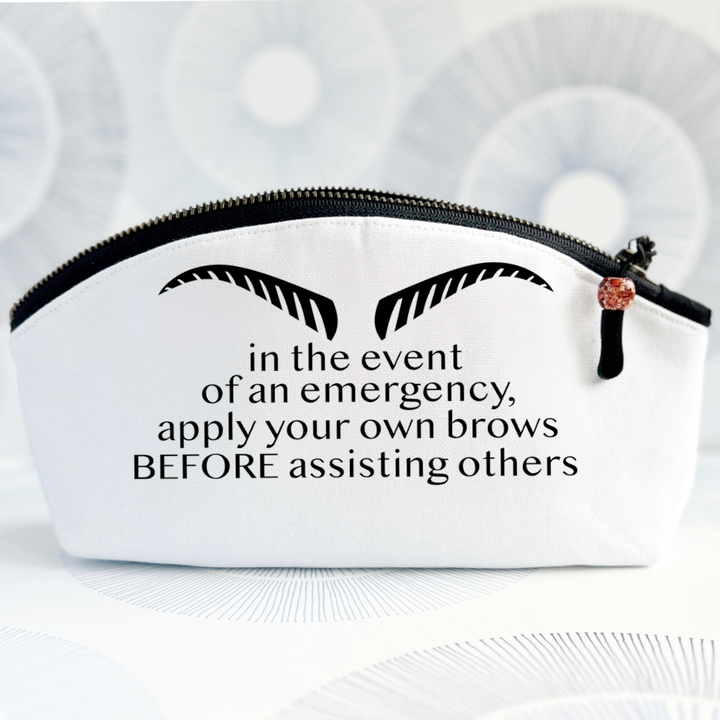 white canvas bag with black zipper, strong eyebrows and the words, in the event of an emergency, apply your own brows BEFORE assisting others