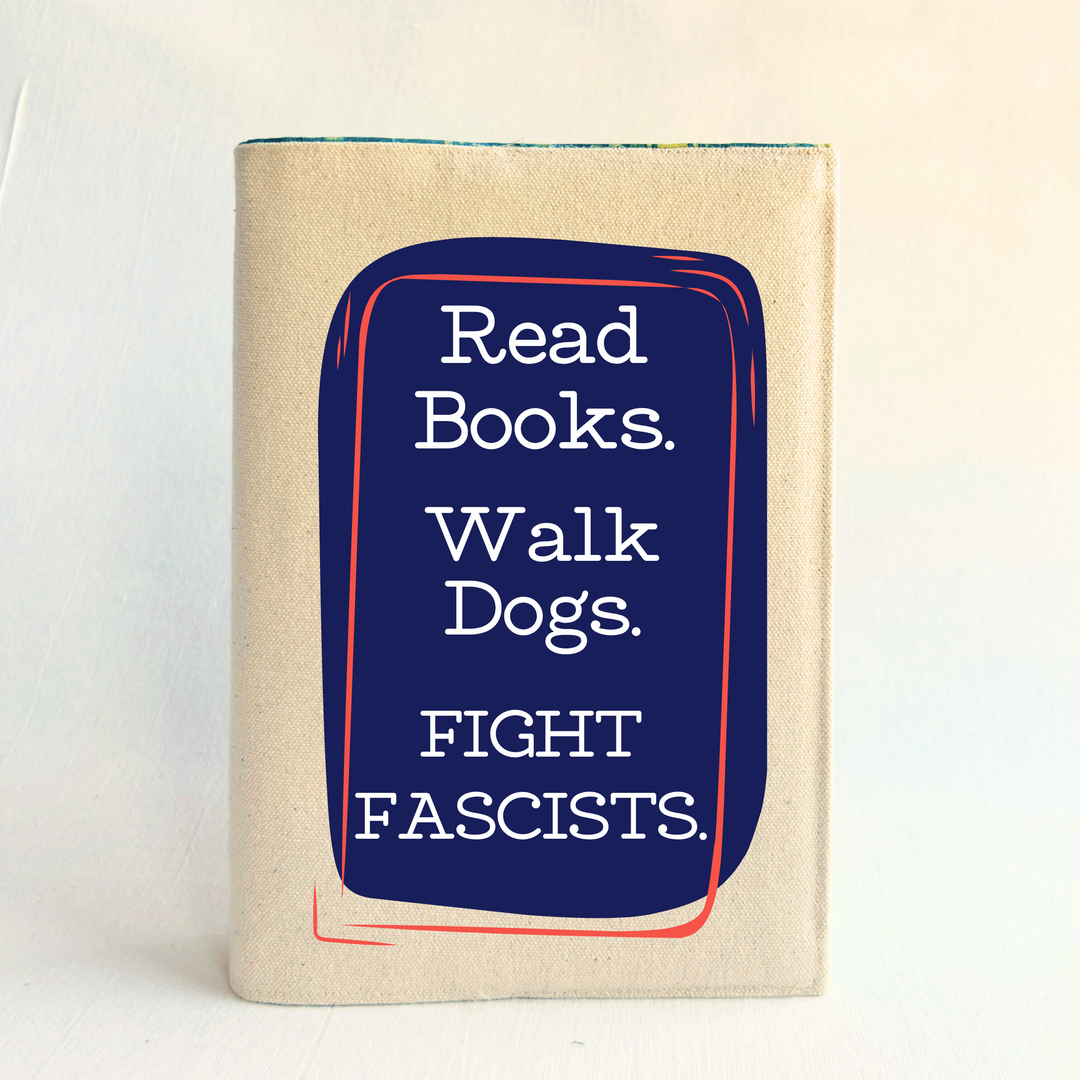 A canvas, reusable book cover in linen, with the words, 'Read Books. Walk Dogs. FIGHT FASCISTS.'  in white lettering placed on a rectangular navy box design.