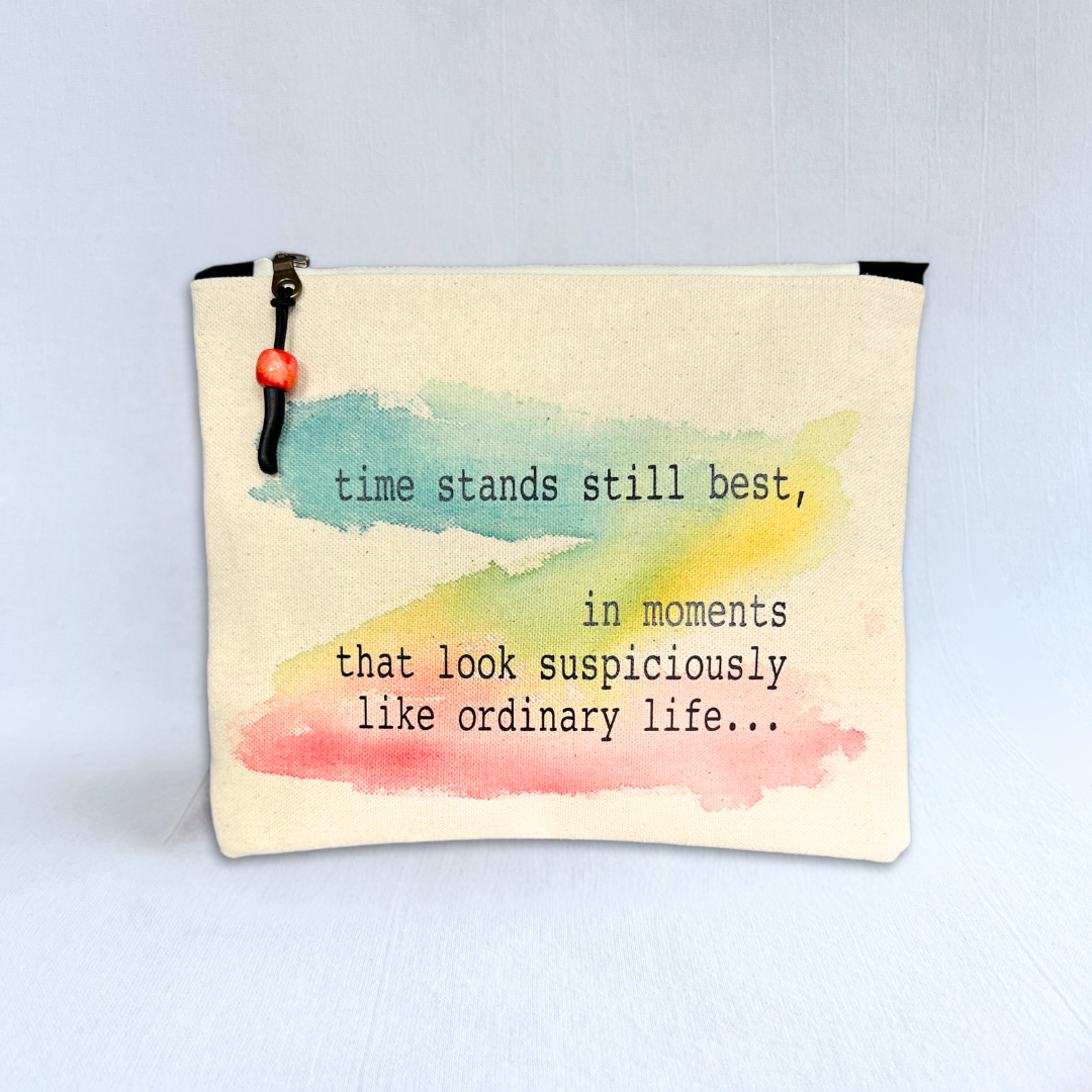 rectangular canvas bag with a zipper pull, in linen-colored duck cloth canvas. Watercolor paint in blues, yellows and reds is the background for the words, time stands still best, in moments that look suspiciously like ordinary life...
